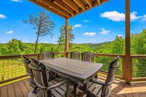 Een houten terras met tafel en stoelen, met uitzicht op een weelderig groen landschap.