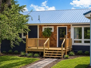 Une maison avec une terrasse en bois, une porte dotée d’une fenêtre et un toit en métal.