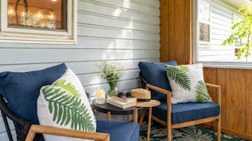 A cozy seating area with two blue chairs, a small table with a vase of flowers, and a window with a view of the outside.