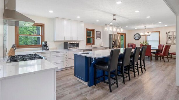 A modern kitchen with white cabinets, a blue island, and a dining area with red chairs.