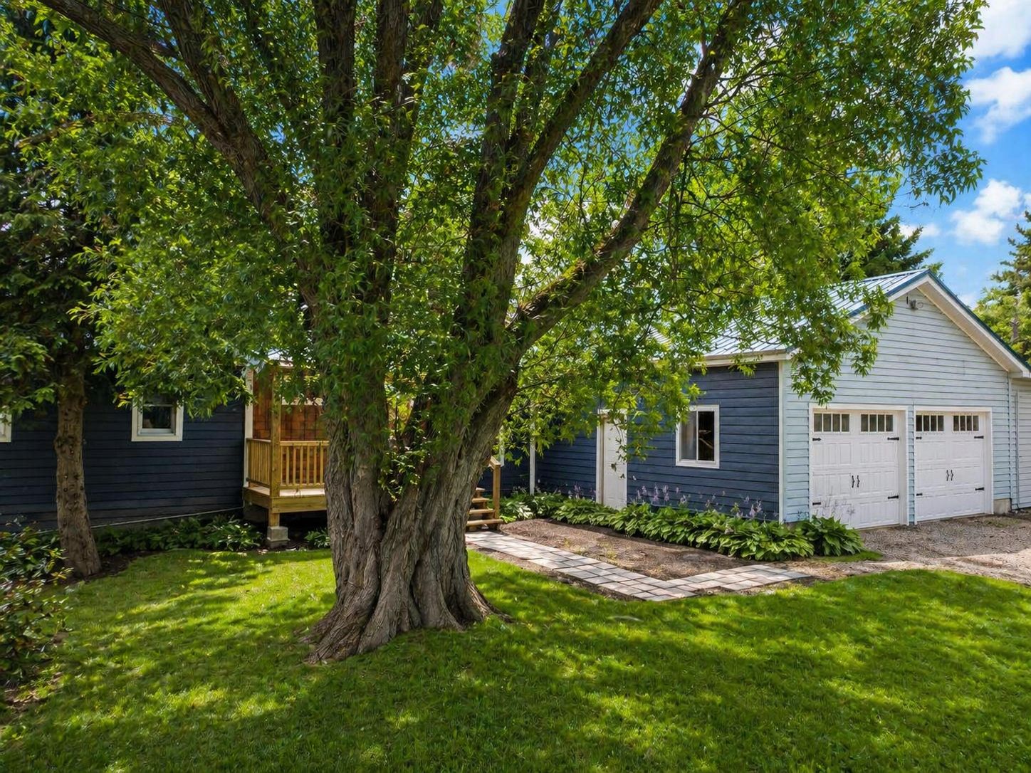 A house with a large tree in the front yard, a wooden deck, and a garage.
