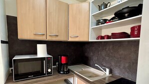 A compact kitchen with a microwave, coffee maker, sink, and wooden cabinets. - Spacious apartment with pool, 5-minute walk from the beach (Le Gosier)