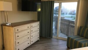 A hotel room with a wooden dresser, a flat-screen TV, a striped sofa, and a sliding glass door to the outside.
