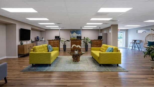 A spacious room with two yellow sofas, a wooden coffee table, and a TV on the wall.