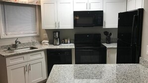 A kitchen with white cabinets, a black microwave, a black refrigerator, and granite countertops.