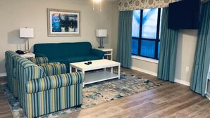 A living room with a teal sofa, striped armchairs, a white coffee table, and a large window with curtains.