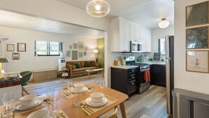 Une cuisine moderne avec des meubles blancs, un réfrigérateur en acier inoxydable et un coin repas doté d’une table en bois, mise pour quatre personnes.