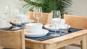 A wooden dining table set with white plates, bowls, and clear glasses, accompanied by gold cutlery.