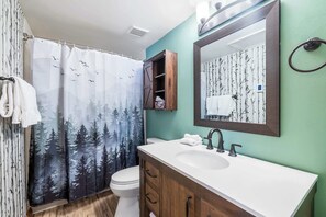 A bathroom with a white sink, wooden cabinets, a mirror, and a shower curtain with a forest design. - Trail Ridge Retreat Sleeps 8 (Edwards)