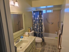 A bathroom with a sink, toilet, and bathtub. There is a shower curtain with a floral pattern, and a towel rack with towels. - Furnished 1900sf 3bedr house in downtown Sidney one block from Ocean and shops (Sidney)