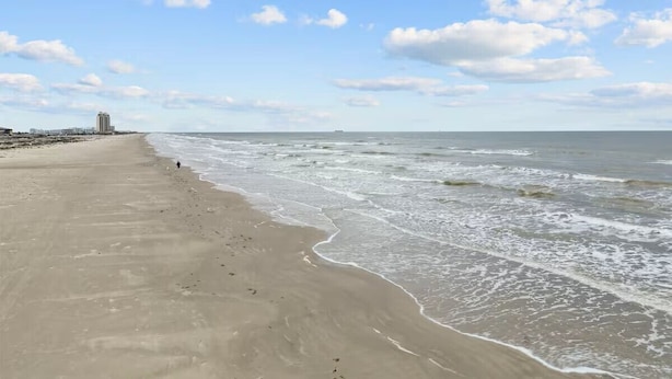 Ein Strand mit einer weiten Sandfläche, ein paar Gebäuden in der Ferne und dem Ozean.