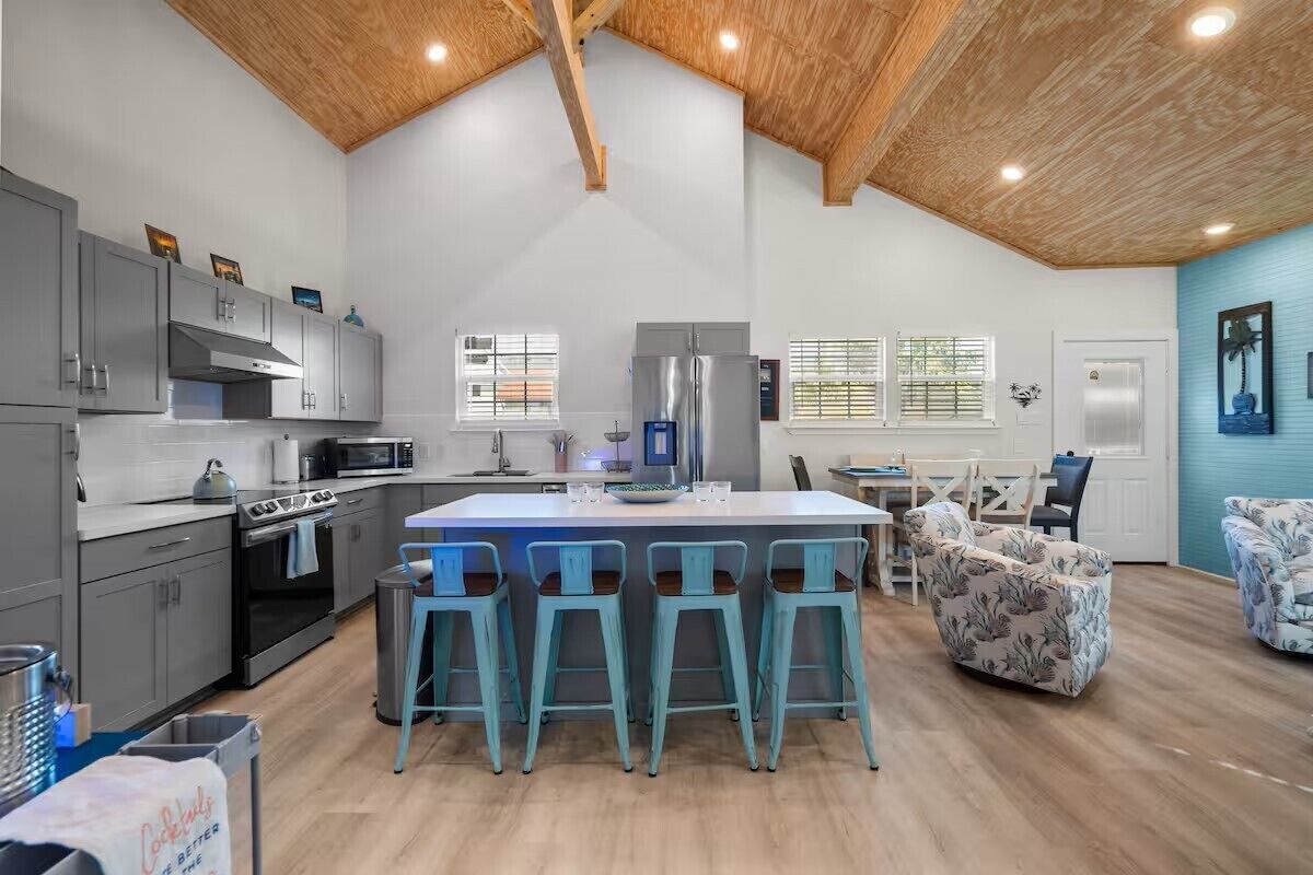 A modern kitchen with grey cabinets, a central island with bar stools, and a wooden ceiling.