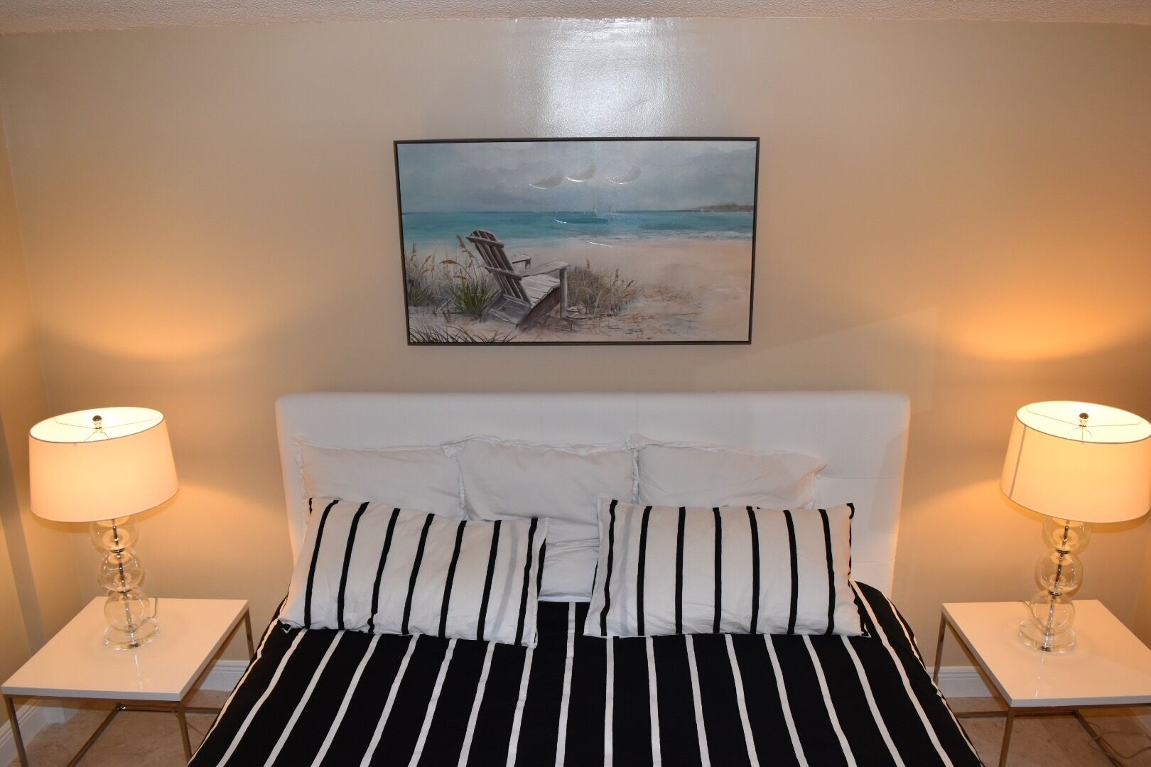 Ein Bett mit schwarz-weiß gestreifter Bettwäsche, zwei Nachttischlampen und ein Strandbild an der Wand.