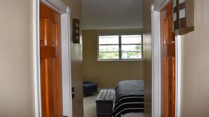 A narrow hallway leading to a bedroom with a window, a bed, and a bench. - APARTAMENTO ENTERO REFORMADO A NUEVO (Sunny Isles Beach)