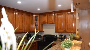 A kitchen with wooden cabinets, a stove, a microwave, and a sink. There are plants on the counter and a fruit bowl with bananas. - APARTAMENTO ENTERO REFORMADO A NUEVO (Sunny Isles Beach)