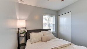 A bedroom with a bed, a nightstand with a lamp, a window, and a wardrobe.