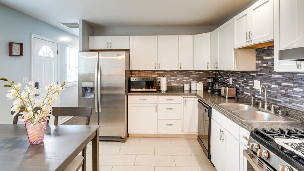 A modern kitchen with white cabinets, a stainless steel refrigerator, a built-in oven, a gas stove, and a tiled backsplash.
