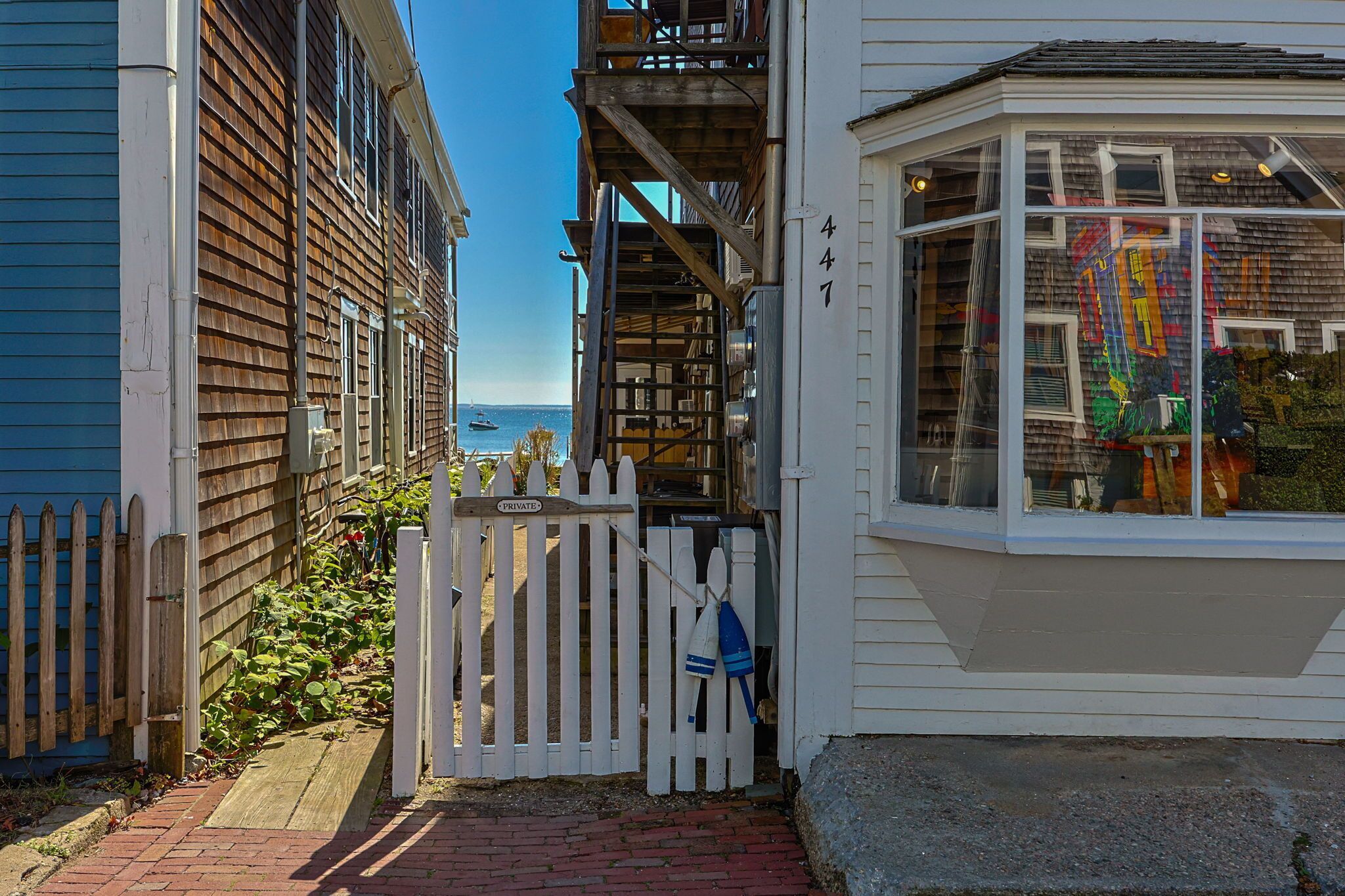 Un étroit sentier mène à un bâtiment blanc doté d’une baie vitrée et d’une clôture en bois.