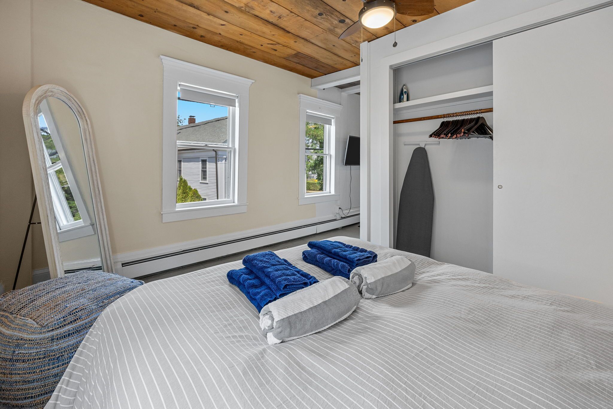 Ein Schlafzimmer mit einem Bett, zwei Fenstern, einer Holzbalkendecke, einem Kleiderschrank und einem Spiegel.