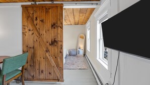 Une pièce avec un plafond en bois, une grande porte coulissante de style grange, une grande fenêtre et un téléviseur fixé au mur.
