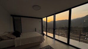 A modern bedroom with a large bed, a view of a cityscape, and a patterned rug. - Only 30 min from Trujillo: Luxury retreat in the mountains ideal for disconnecting (Simbal)