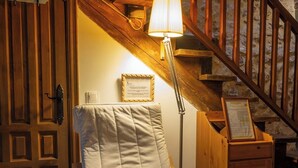 Une chaise en bois avec un coussin, dans une pièce dont le mur est en pierre et qui possède un escalier en bois.