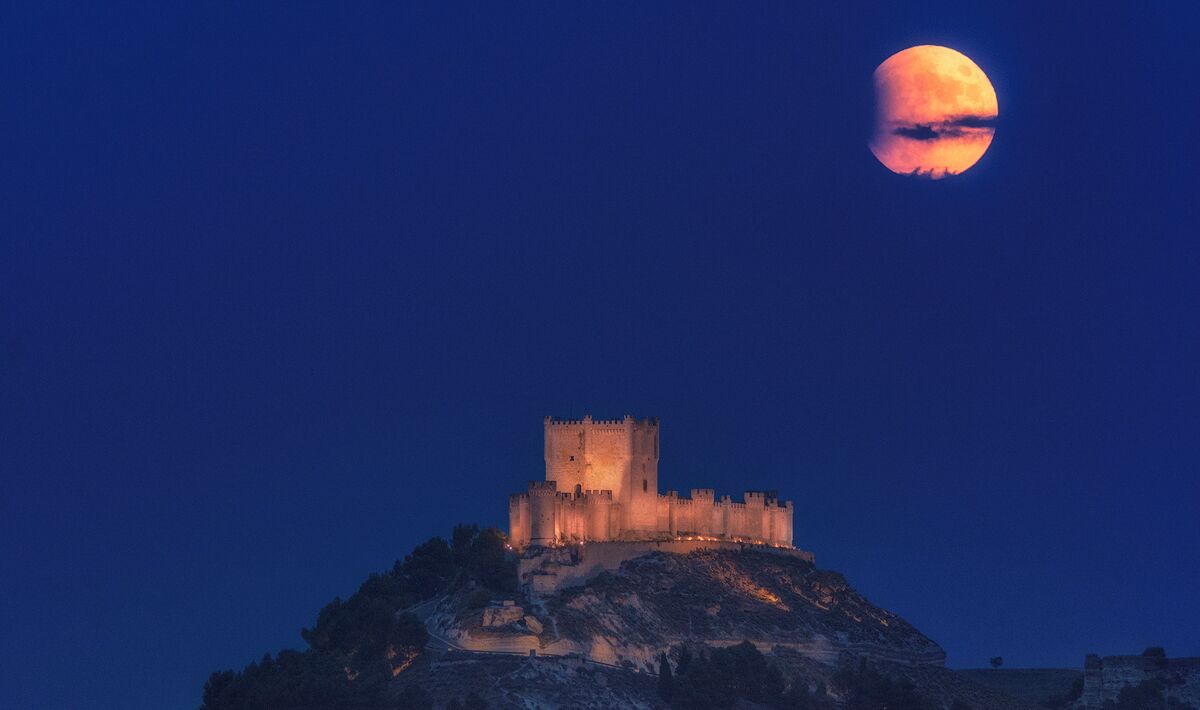 Un castillo en una colina bajo una luna llena.