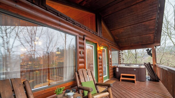 A wooden deck with a hot tub, a wooden chair, and a table with a plant and a bucket.