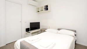 A modern hotel room with a bed, a TV, a small table, and a shelf with plants. - Ticinese 28 Apartment (MILANO)