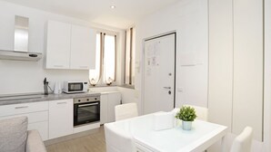 A modern kitchen with white cabinets, a microwave, and an oven. There is a dining table with chairs and a small potted plant. - Ticinese 28 Apartment (MILANO)