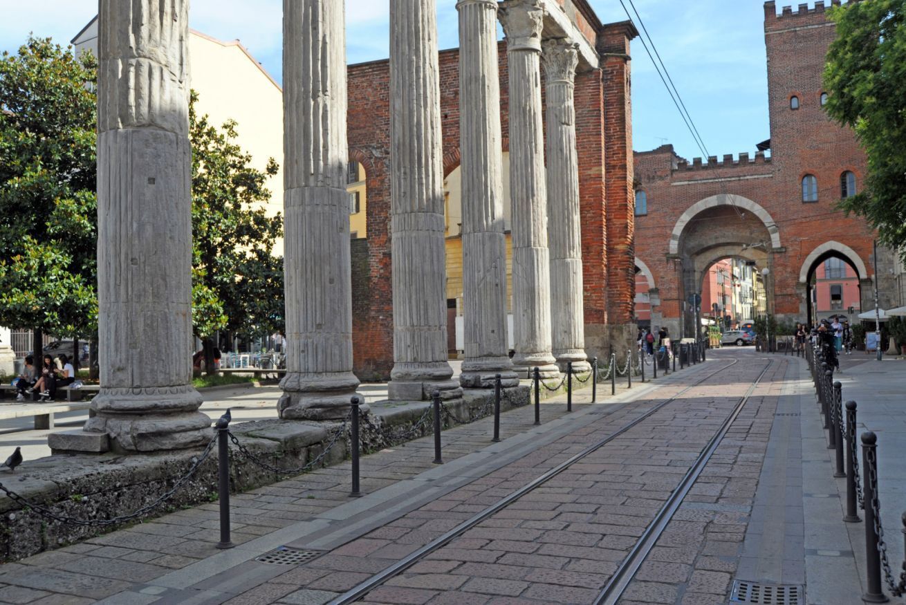 A street with ancient columns, a brick building, and a tram track.
