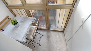 A small, narrow room with a bed, a plant, and a window. - Ticinese 28 Apartment (MILANO)