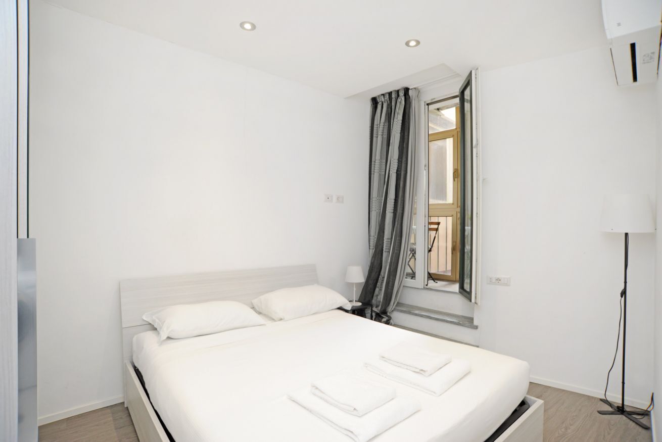 Ein modernes Hotelzimmer mit einem großen Bett, einem Fenster mit Vorhängen, einem Nachttisch und einer Stehlampe.