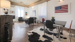 A living room with a glass table, black chairs, a cowhide rug, a TV, and a flag on the wall.
