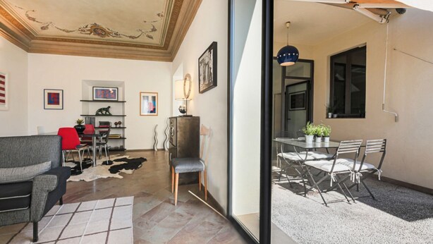 A living room with a sofa, chairs, a dining table with chairs, a ceiling with decorative molding, and a view of an outdoor patio area.