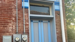 A grey door with blue decorative elements, a brick wall, and electrical boxes.