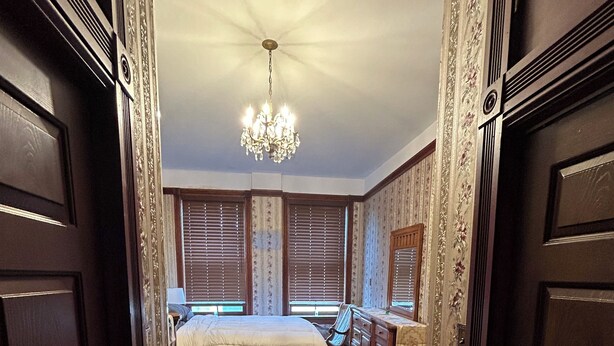 A bedroom with a large bed, wooden wardrobe, and a chandelier.
