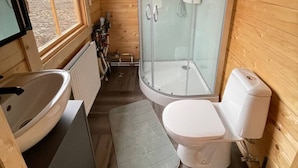 Ein Badezimmer einer Holzhütte mit einer Duschkabine aus Glas, einem Waschbecken und einer Toilette.