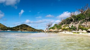 Una playa con aguas poco profundas y transparentes, un litoral arenoso y afloramientos rocosos con vegetación escasa.