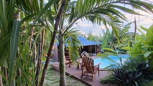 A pool area with wooden deck chairs and a small building in the background. - KAZ A KLEMENCE - Gite colibris : Haven of peace with swimming pool & local cuisine (Anse-Bertrand)