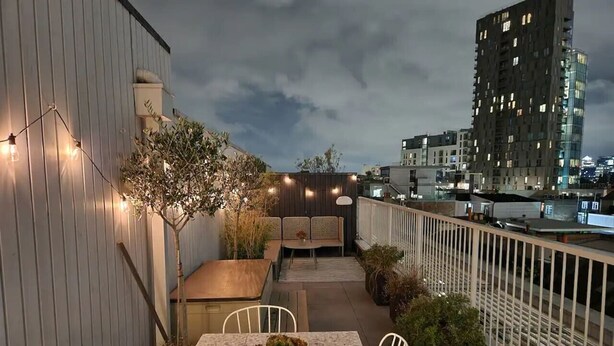 An outdoor terrace with a table and chairs, string lights, and potted plants.