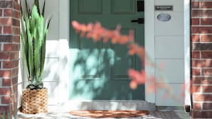 A green door with a "Lantern House" sign, a doormat, and a potted plant on the porch.