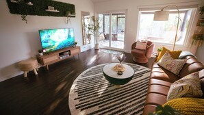 A modern living room with a flat-screen TV, a brown leather sofa, a round coffee table, and a large window.
