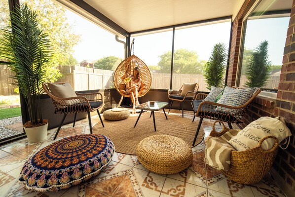 A sunlit patio with wicker furniture, a patterned cushion, and a potted plant.