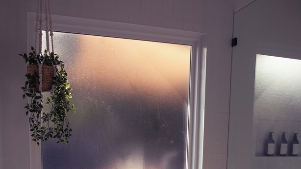 A bathtub with a window, a bottle, and a glass.