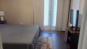 A bedroom with a bed, a TV, a desk, and a window with curtains.