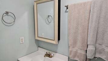 Une salle de bain avec un lavabo blanc, un miroir avec un cadre en bois et deux serviettes suspendues à un porte-serviettes.