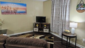 A living room with a television, a sofa, a coffee table, and a decorative wall hanging.