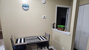 A dining area with a table and chairs, a clock on the wall, a window with a view, and a door.