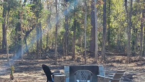 A rustic outdoor seating area with a fire pit, surrounded by trees.